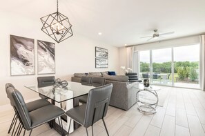 Ein modernes Wohnzimmer mit einem Glastisch, grauen Sofas und einem Deckenventilator.