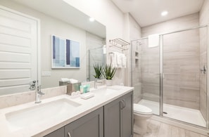 A modern bathroom with a glass shower enclosure, a white sink, and a large mirror. - The Tranquil Townhome - Elegant Townhome in Reunion Resort (Kissimmee)