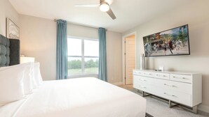 Ein Schlafzimmer mit einem großen Bett, einem Deckenventilator, einem weißen Schminktisch, einem Gemälde und einem Fenster mit Vorhängen.