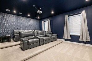 Ein Heimkino mit dunkelblauer Wand, einem grauen Ledersofa und Teppichboden.