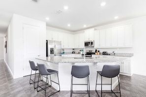 A modern kitchen with white cabinets, a granite countertop, and three bar stools. - Magical Villa With Themed Bedrooms at Reunion (Kissimmee)