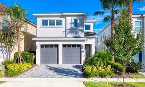 A two-story residential building with a garage, surrounded by well-maintained landscaping and palm trees. - Magical Villa With Themed Bedrooms at Reunion (Kissimmee)