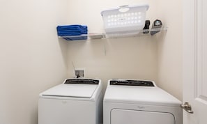 A laundry area with two front-loading washing machines, a drying rack, and a folded blue towel on a shelf. - Luxurious Villa With Tiki Themed Game Room at Encore (Kissimmee)