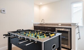 Ein Zimmer mit Tischfußballtisch, einer Küchenzeile inklusive Herd und einem Fenster mit Jalousien.