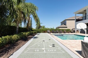 Ein Shuffleboard-Spielfeld neben einem Pool mit Liegestühlen und einem Gebäude im Hintergrund.