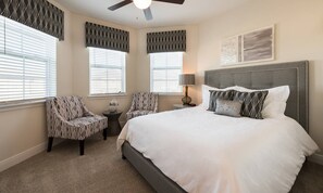 Ein Schlafzimmer mit einem großen Bett, zwei Sesseln, einem Nachttisch und einem Deckenventilator.