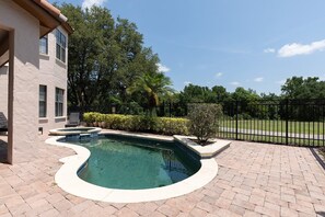 A swimming pool with a curved design, surrounded by a brick patio, and a fence enclosing a grassy area. - Happy Abode With Annex at Reunion (Kissimmee)