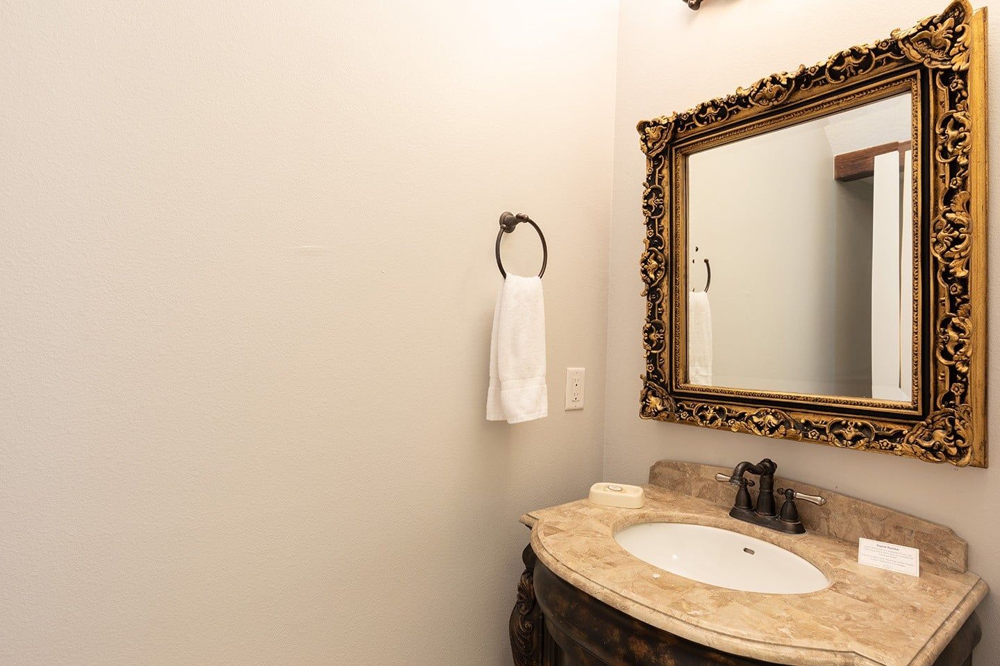 A bathroom with a marble sink, a gold-framed mirror, and a towel hanging on a hook.