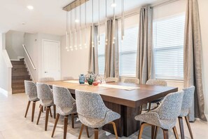 A dining area with a rectangular table, six upholstered chairs, hanging pendant lights, and a staircase in the background. - Exquisite Home w/ Games Room at Encore (Kissimmee)