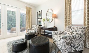 Ein Wohnzimmer mit einer Couch, Poufs, einem Sessel, einer Lampe und einem Spiegel.