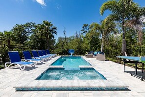 Ein rechteckiger Swimmingpool mit einer bepflasterten Kante, umgeben von Liegestühlen und einem Tischtennis-Tisch.
