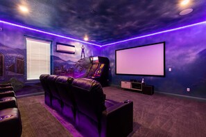 Ein Heimkino mit großer Leinwand, bequemen Sitzgelegenheiten und einer Spielkonsole.