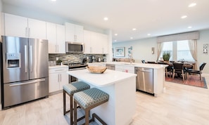 A modern kitchen with stainless steel appliances, a central island with stools, and a dining area with a view. - Sun-kissed Villa With Private Pool at Encore (Kissimmee)