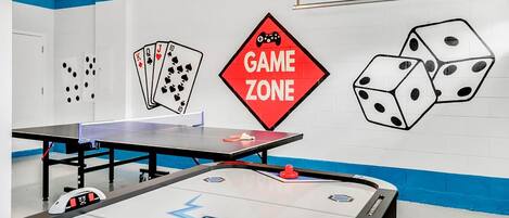 A room with a ping pong table, a foosball table, and a wall with a 'GAME ZONE' sign.