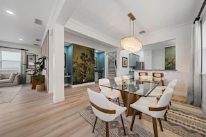 A modern dining area with a glass table and white chairs, a kitchen with blue cabinets, and a living room with a sofa and plants. - Tropical Retreat With Screened in Private Pool and Spa at Reunion (Kissimmee)
