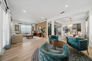 A spacious living room with a sofa, a coffee table, and a dining area with chairs. - Tropical Retreat With Screened in Private Pool and Spa at Reunion (Kissimmee)