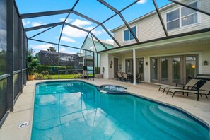 A swimming pool with a hot tub, surrounded by a covered patio area with chairs and a view of a house. - Tropical Retreat With Screened in Private Pool and Spa at Reunion (Kissimmee)