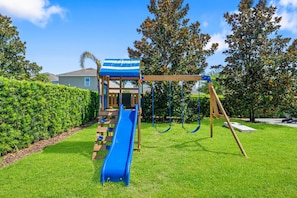 Ein Spielplatz mit Rutsche, Schaukeln und einem überdachten Spielhäuschen.
