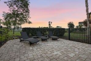 An outdoor patio with lounge chairs and a paved floor, surrounded by a fence and greenery. - Upscale Oasis With Home Theater at Reunion (Kissimmee)