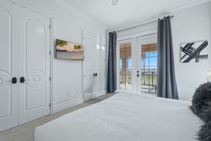 A bedroom with a large bed, white walls, a painting, and a view through a glass door. - Upscale Oasis With Home Theater at Reunion (Kissimmee)
