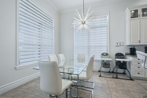 A modern kitchen with white cabinetry, a glass dining table, and two high chairs. - Upscale Oasis With Home Theater at Reunion (Kissimmee)