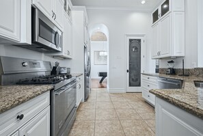 A modern kitchen with white cabinetry, granite countertops, stainless steel appliances, and a tiled floor. - Upscale Oasis With Home Theater at Reunion (Kissimmee)