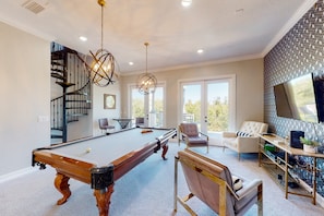 A spacious living room with a pool table, a comfortable seating area, and a staircase leading to an upper level. - Luxury Villa With Elegant Living Space at Reunion (Kissimmee)