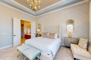 A spacious bedroom with a large bed, a bedside table with a lamp, a chair, and a mirror on the wall. - Luxury Villa With Elegant Living Space at Reunion (Kissimmee)