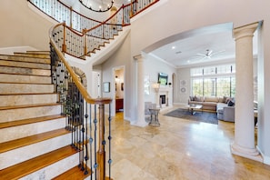 A spacious living area with a grand staircase, a fireplace, and a modern ceiling fan. - Luxury Villa With Elegant Living Space at Reunion (Kissimmee)
