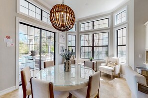 A dining area with a glass table, white chairs, and a hanging light fixture. - Luxury Villa With Elegant Living Space at Reunion (Kissimmee)