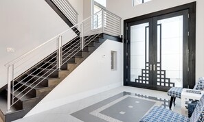 Ein modernes Interieur mit einer Treppe, einer großen Schiebeglaswand und einer Sitzecke mit gemusterten Kissen.
