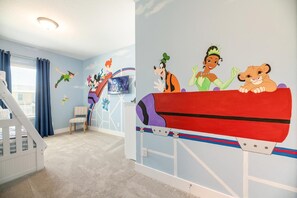 Ein Kinderzimmer mit farbenfrohem Wandbild, einem Spielstall und einem Fernseher.