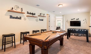 A pool table with a billiards cue, a foosball table, and wall decorations for sports like basketball, baseball, football, soccer, and golf. - Sleek Residence With Theater Room at Reunion (Kissimmee)
