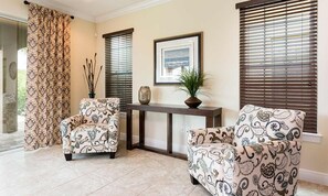 Een kamer met twee gestoffeerde fauteuils, een console tafel met decoratieve objecten, en een groot raam met zonwering.