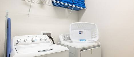 A laundry area with a washing machine, dryer, and a drying rack with folded towels.