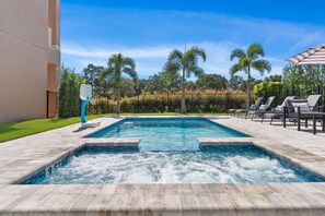 Ein rechteckiger Pool mit einer Hydromassage-Wanne in der Mitte, umgeben von einer gefliesten Terrasse.