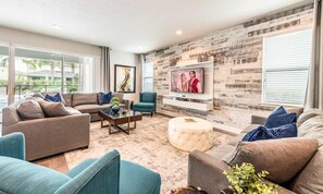 A modern living room with a large TV, comfortable seating, and a rustic brick wall. - Large Spacious Villa With Private Pool and Water Slide at Encore (Kissimmee)