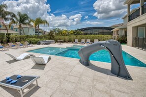 A swimming pool area with lounge chairs, a table, and a poolside table. - Large Spacious Villa With Private Pool and Water Slide at Encore (Kissimmee)