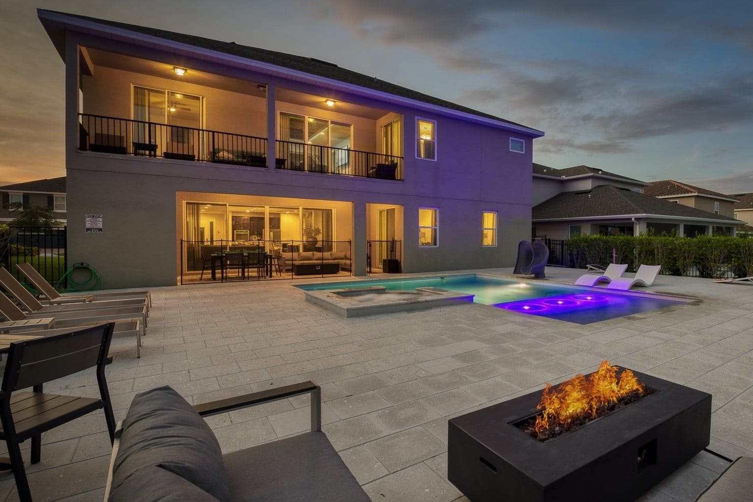 Una casa de dos pisos con piscina, mobiliario exterior y una chimenea.