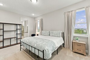 Ein Schlafzimmer mit Bett, Nachttisch, einem Fenster mit Vorhängen, einem Kleiderschrank und einem durchgegangene Tür erkennbaren Badezimmer.