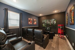 A home theater room with leather recliners, a red arcade machine, and movie posters on the wall. - Encore Resort Villa With Pool & Spa (Kissimmee)