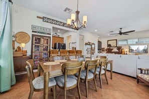 A dining area with a wooden table and chairs, a chandelier, and a kitchen in the background. - Safari Explorer's Retreat w/ Theme Decor Private Pool (Kissimmee)