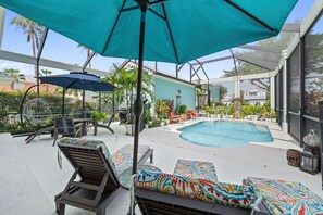 A pool area with lounge chairs and umbrellas, surrounded by a fence and various plants. - Safari Explorer's Retreat w/ Theme Decor Private Pool (Kissimmee)