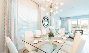 A modern dining area with a glass table, white chairs, and a decorative ceiling light. - Modern 6 Bedroom Home With Upscale Living at Reunion (Kissimmee)