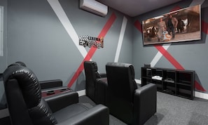 A home theater room with black leather chairs, a large flat-screen TV, and a wall-mounted projector. - Modern 6 Bedroom Home With Upscale Living at Reunion (Kissimmee)