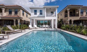 A swimming pool with lounge chairs and a dining area, surrounded by two-story buildings with balconies. - Modern 6 Bedroom Home With Upscale Living at Reunion (Kissimmee)