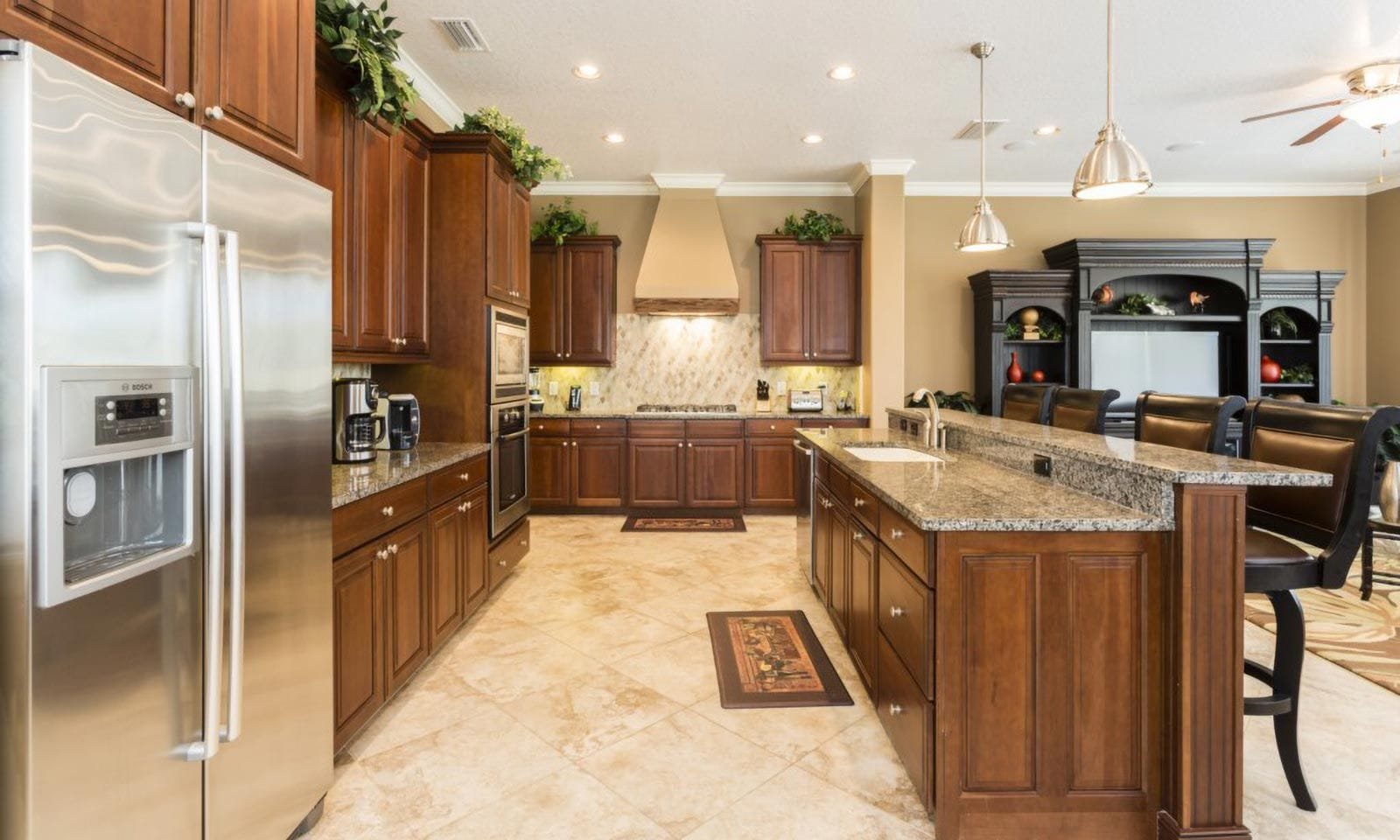 A spacious kitchen with wooden cabinets, a stainless steel refrigerator, a granite countertop island, and a built-in oven.