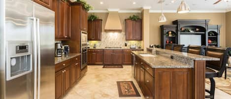 A spacious kitchen with wooden cabinets, a stainless steel refrigerator, a granite countertop island, and a built-in oven.