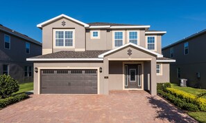 A two-story residential building with a garage, a front door, and a small porch area. - Stylish Sleek Home With Full Kitchen at Encore (Kissimmee)