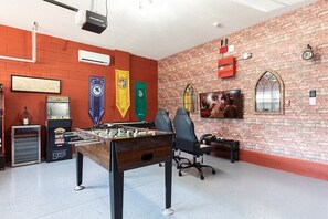 A room with a foosball table, gaming chairs, a television, and a brick wall. - Stylish Sleek Home With Full Kitchen at Encore (Kissimmee)